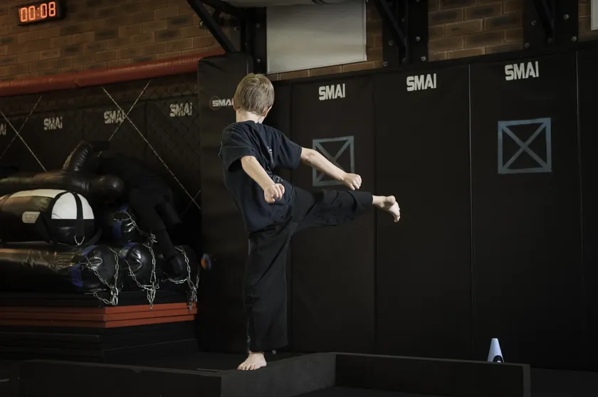 A Little Dragons student holding a high side kick on the balance beam