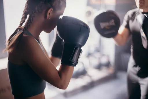 Woman in black sportswear punches focus mitts with a trainer in a bright gym, focused and intense.