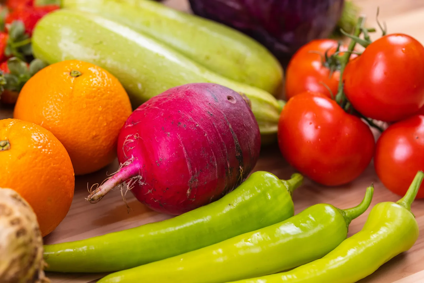 Close-up of colorful fresh produce on a table: oranges, tomatoes, peppers, a red beet, and pale green squash.