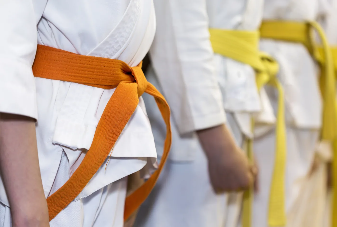 Close-up of martial arts students in white gis with orange and yellow belts standing in line.
