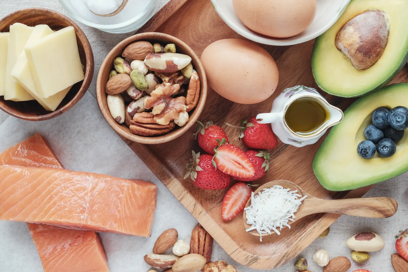 Overhead flat lay of salmon, eggs, avocado, berries, nuts, cheese and oil on wooden boards, fresh breakfast spread.