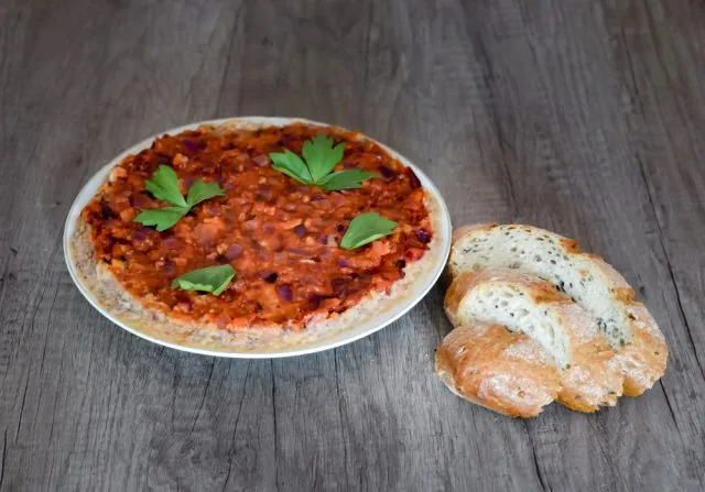 Plate of red tomato dip topped with parsley, served with sliced crusty bread on a rustic wooden table